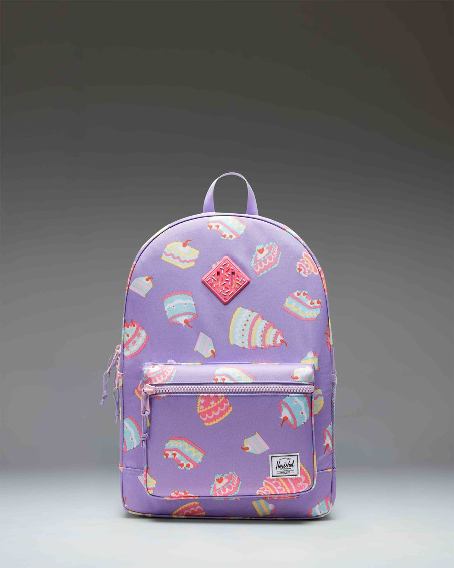 Herschel Heritage Youth Backpack in the Cakes colorway, featuring a playful print pattern with a front pocket and classic woven label.