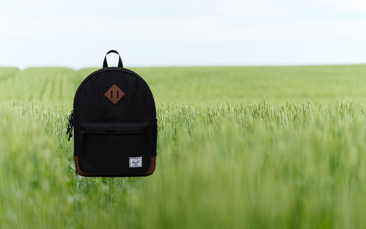 Herschel Heritage Kids Backpack in Black and Saddle Brown, shown from a front lifestyle view on a desktop background.