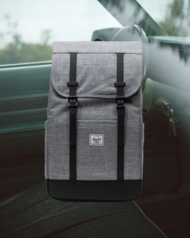 Herschel Retreat Backpack in Raven Crosshatch, showing a front view of the grey fabric bag with black rubber straps and a white logo label.
